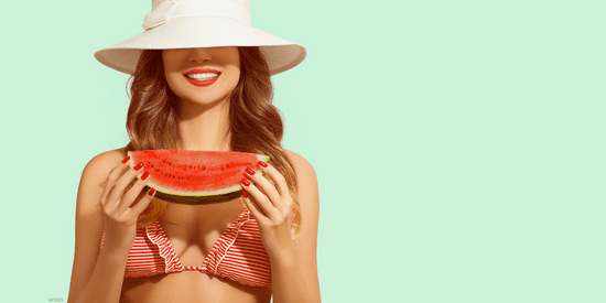 Model in bikini and sun hat holding slice of watermelon