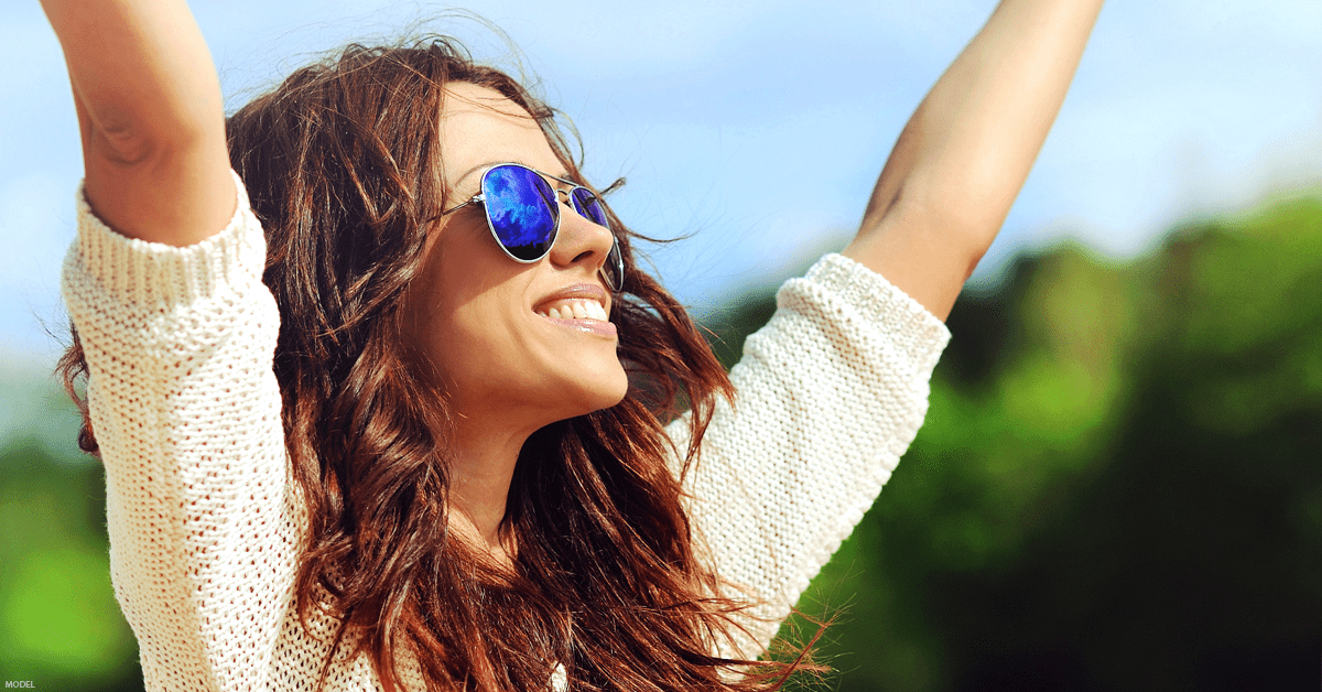 Young woman smiling wearing sunglasses and raising arms in air