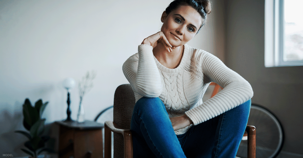 Young woman sitting in chair contemplating EMSCULPT® treatment