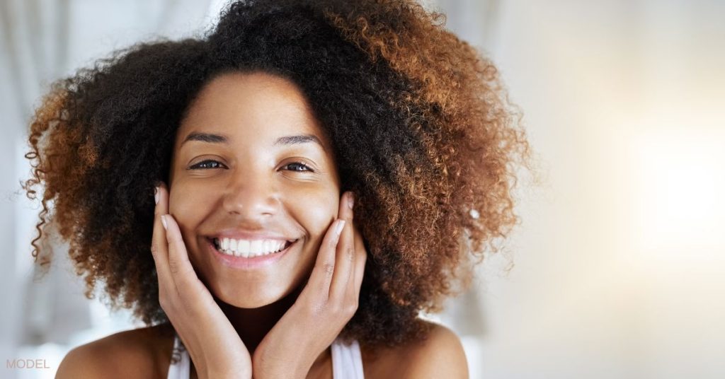 Woman smiling, holding her face in her hands (model)