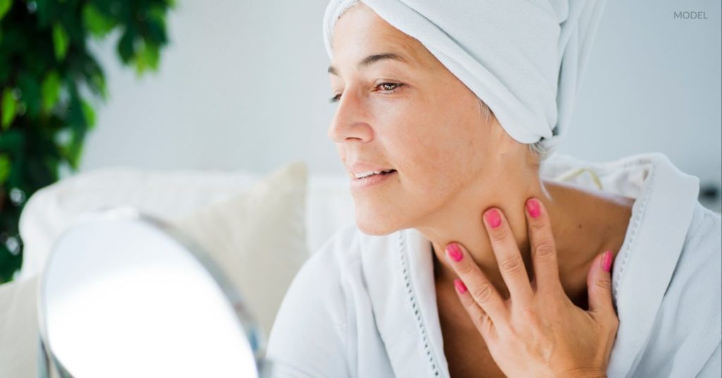 Woman with clear skin and a defined jawline (model) looking in a small mirror.