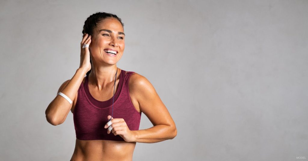 A woman in a sports bra top smiling. (Model)